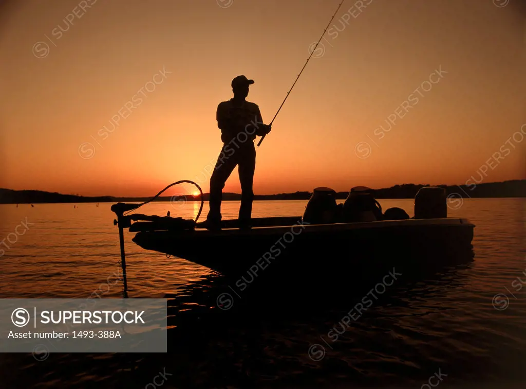 Silhouette of a man standing on a boat and fishing