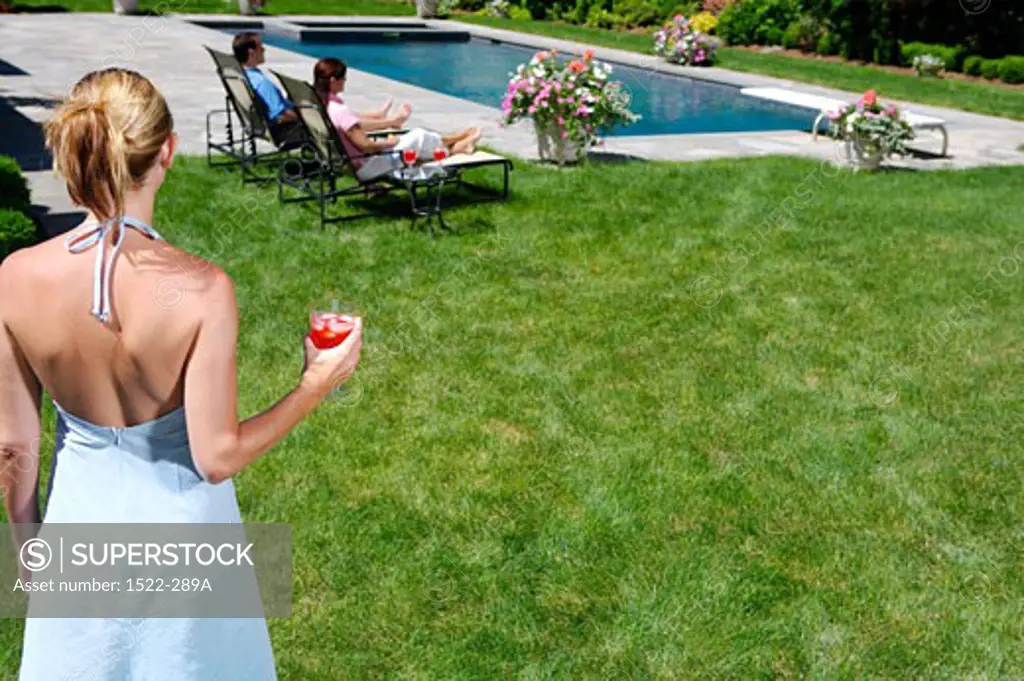 Rear view of a young woman holding a drink and a young couple sitting at poolside