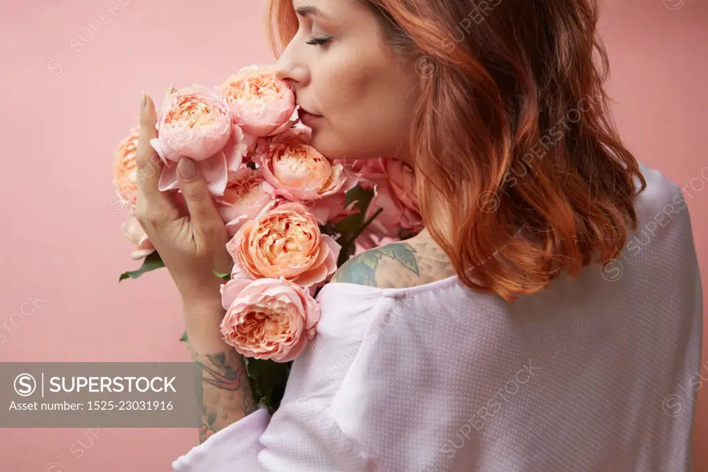 Beautiful girl with fragrant flowers on a background in a trendy color of the year 2019 Living Coral Pantone. Mother&rsquo;s Day and Valentine&rsquo;s Day greeting post cards.. A girl with a tattoo holds a bouquet of flowers roses on a pastel background in a trendy color of the year 2019 Living Coral Pantone. Congratulation card concept.