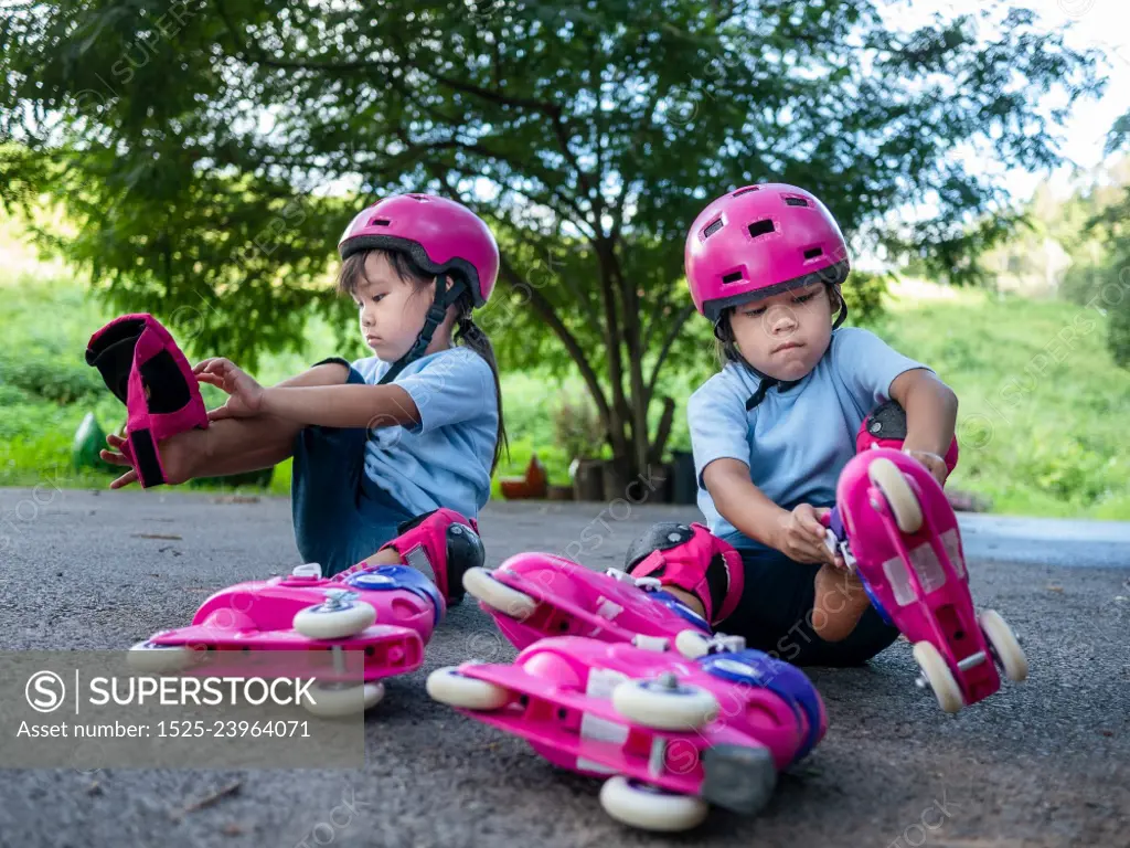 Two sibling sisters wearing protection pads and safety helmet practicing to roller skate on the street in the park. Active outdoor sport for kids.