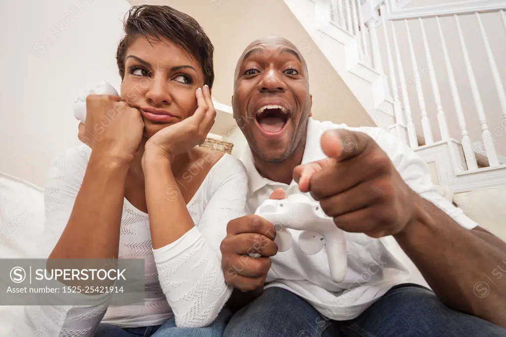 African American couple, man and woman, having fun playing video console games together. The man has just beaten the woman, he is celebrating, she is miserable.