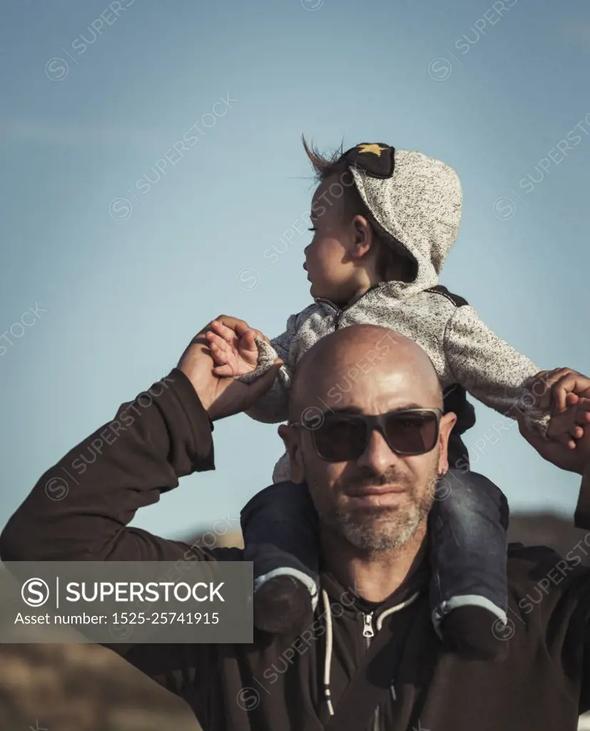 Child is sitting on his father&rsquo;s shoulders, handsome dad playing with his cute little son, enjoying parenthood, family love concept. Happy family life