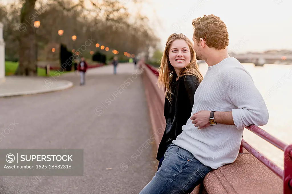 Young couple chatting on waterfront at sunset, Battersea Park, London, UK