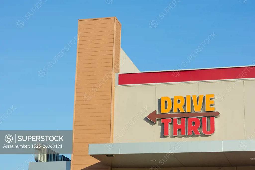 Drive thru sign with left arrow on building against the blue clear sky. Copy space wallpaper.