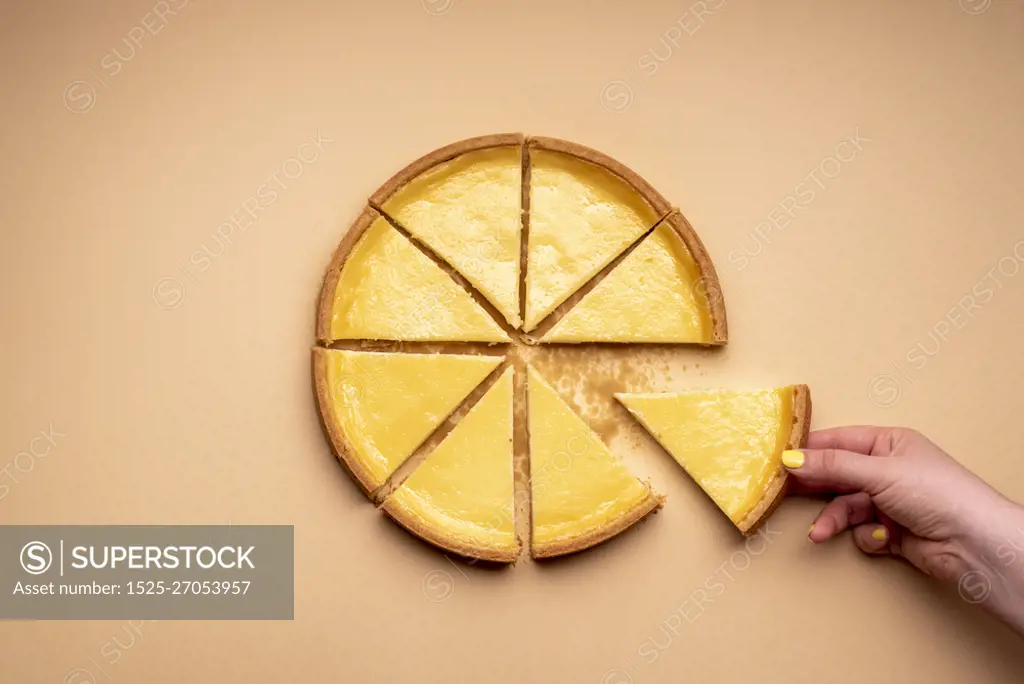 Woman's hand grabbing a piece of cheesecake. Sliced cheese tart on a yellowish background. Pie sliced in equal parts.