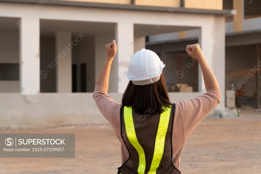 Portrait of an Asian woman engineer construction worker wearing a helmet using a tablet while standing at a construction site. Building Location on the background, Concept of Equality and success