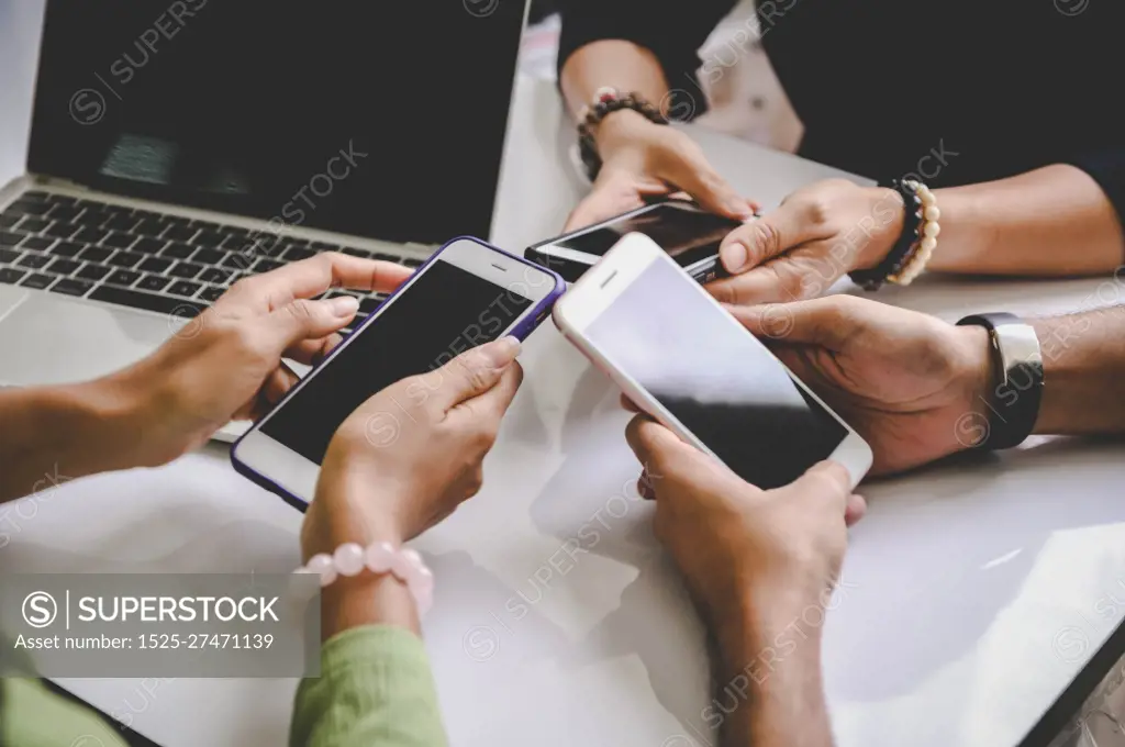 Group of young hipsters holding mobile phones in hands at office with laptop computer background. Friends having fun together with smartphone. Social distancing and work from home concept.