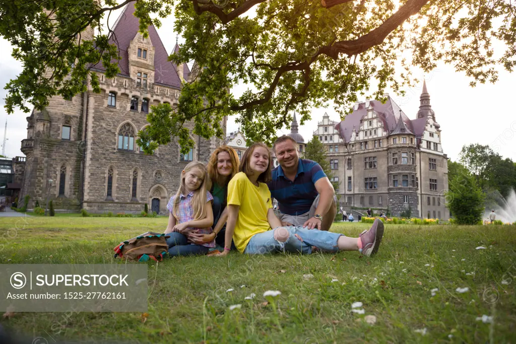 Happy family - mom, dad and two daughters are sitting in a meadow Beautiful castle on the background