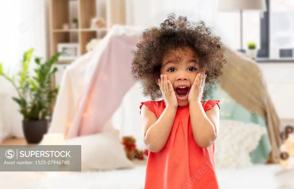 childhood, expressions and emotions concept - surprised or scared little african american girl screaming over kids tent or teepee at home background. surprised or scared little african american girl