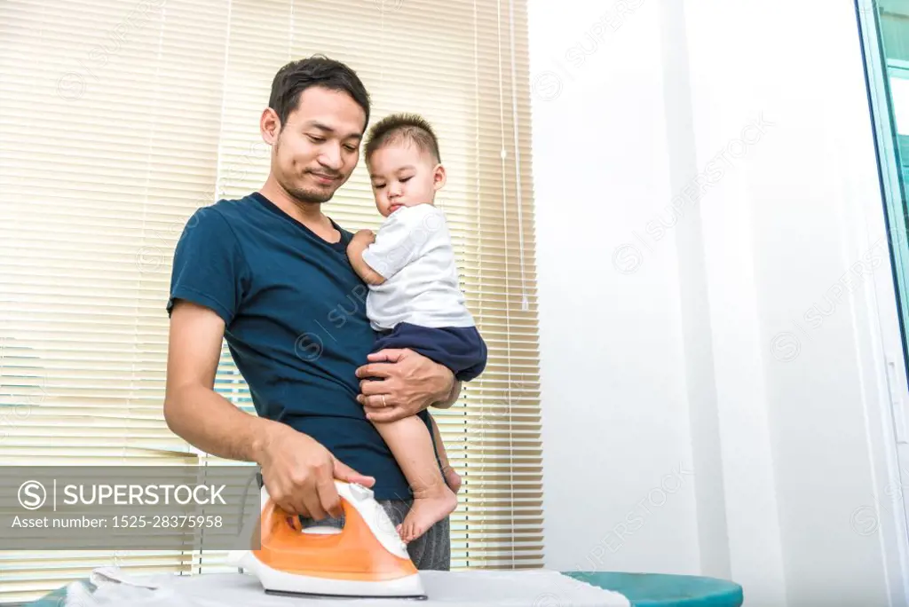 Single dad is ironing while carrying his son. People and Lifestyles concept.