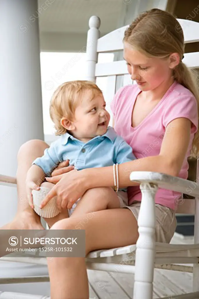 Caucasian pre-teen girl holding male Caucasian toddler looking at each other.