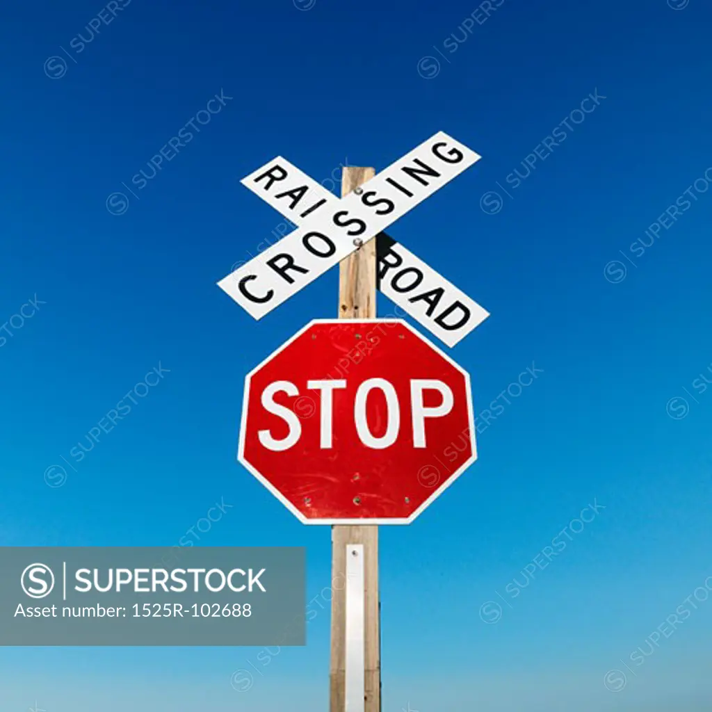 Railroad crossing and stop signs against blue sky.