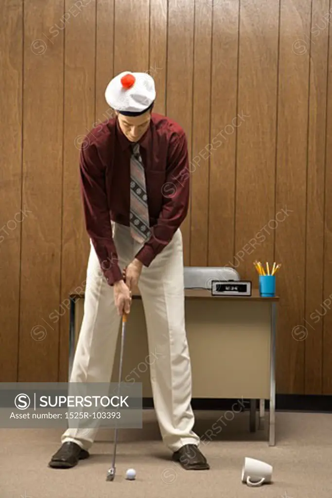 Caucasion mid-adult retro businessman wearing cap putting golf ball into coffee cup in his office.