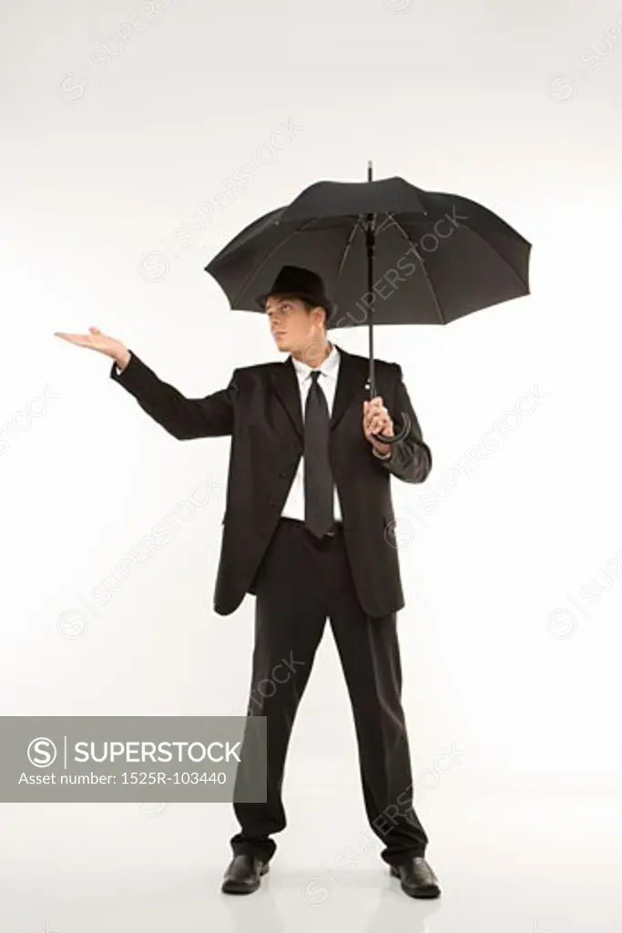 Caucasian mid-adult businessman wearing fedora holding umbrella with arm outstretched.
