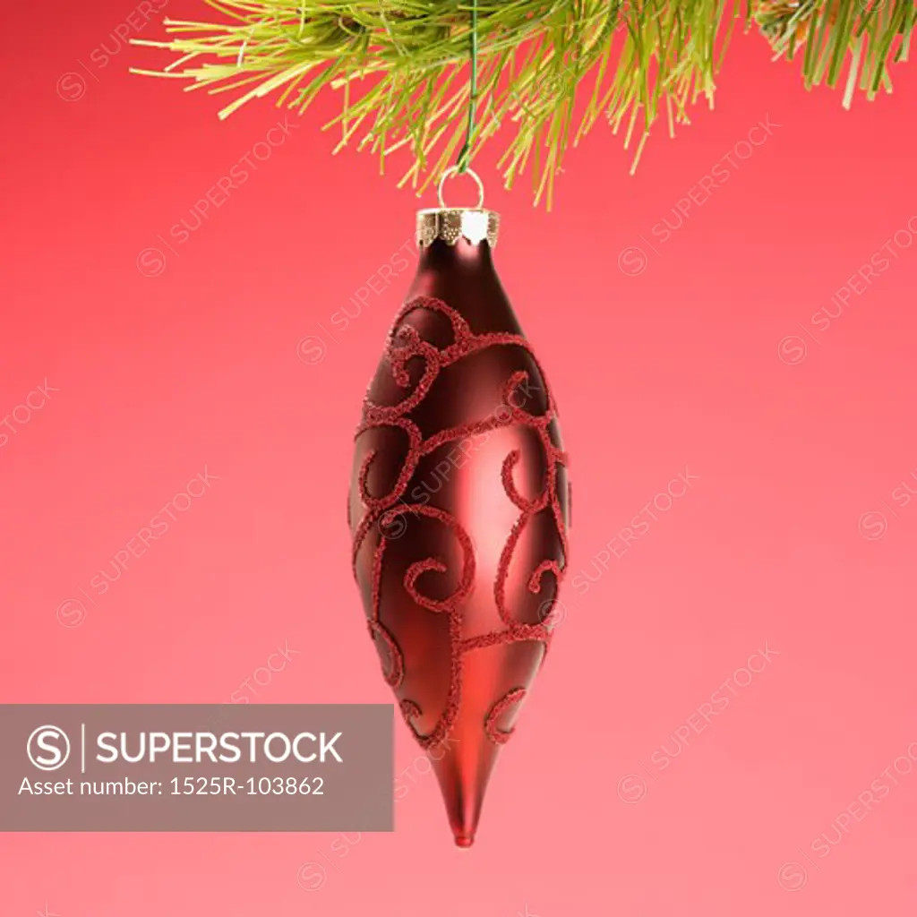 Still life of red Christmas ornament hanging from pine branch.