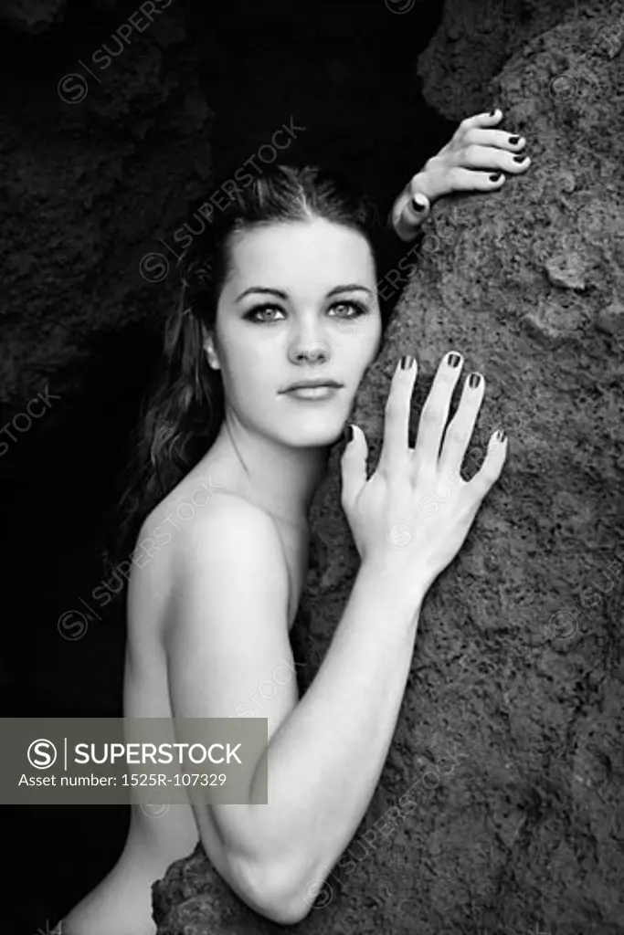 Young nude Caucasian woman leaning against rock and looking at viewer.