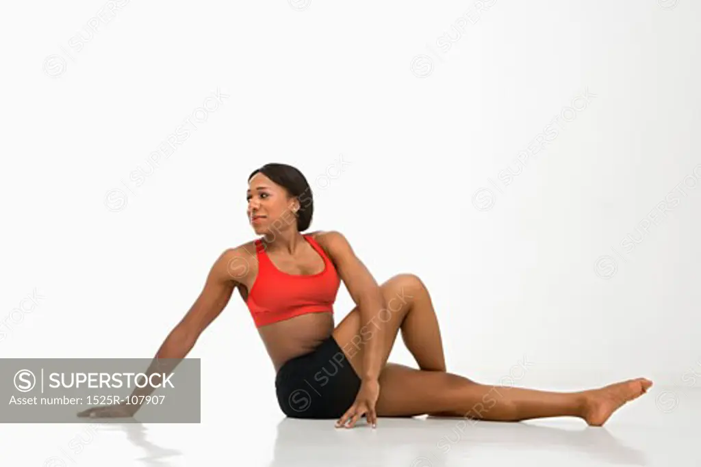 Profile of African American young adult woman stretching on floor.