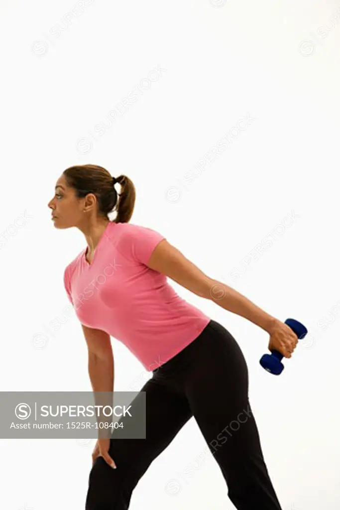 Side view of mid adult multiethnic woman wearing pink shirt exercising with dumbbell.