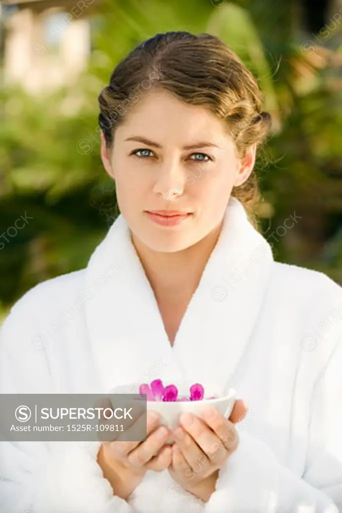 Attractive Caucasian mid-adult woman in white robe holding bowl of purple orchids floating in water.