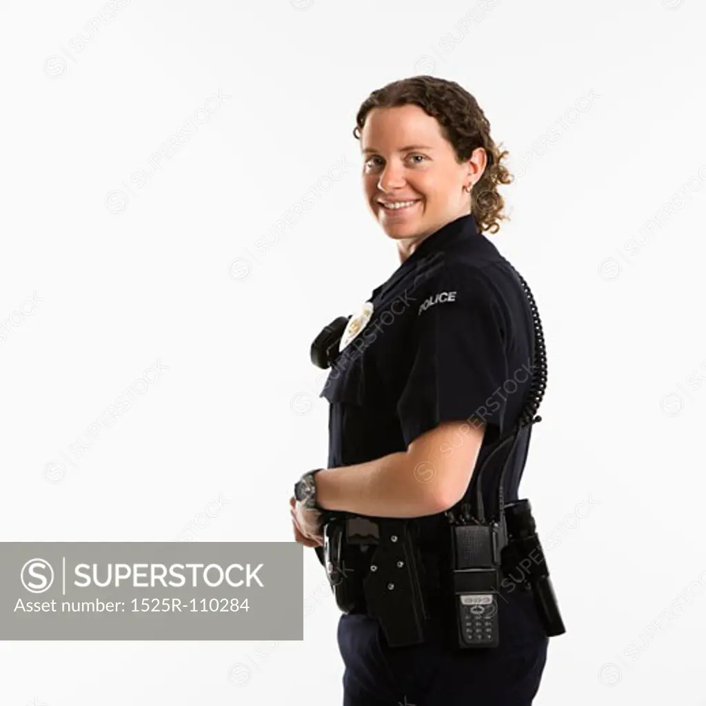 Portrait of mid adult Caucasian policewoman standing with hand on gun holster looking over shoulder at viewer smiling.