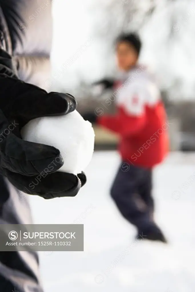 Boy holding snowball ready to throw at boy in background.