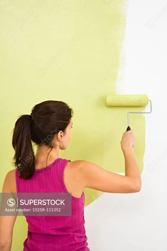 Woman painting interior wall of home with paint roller.