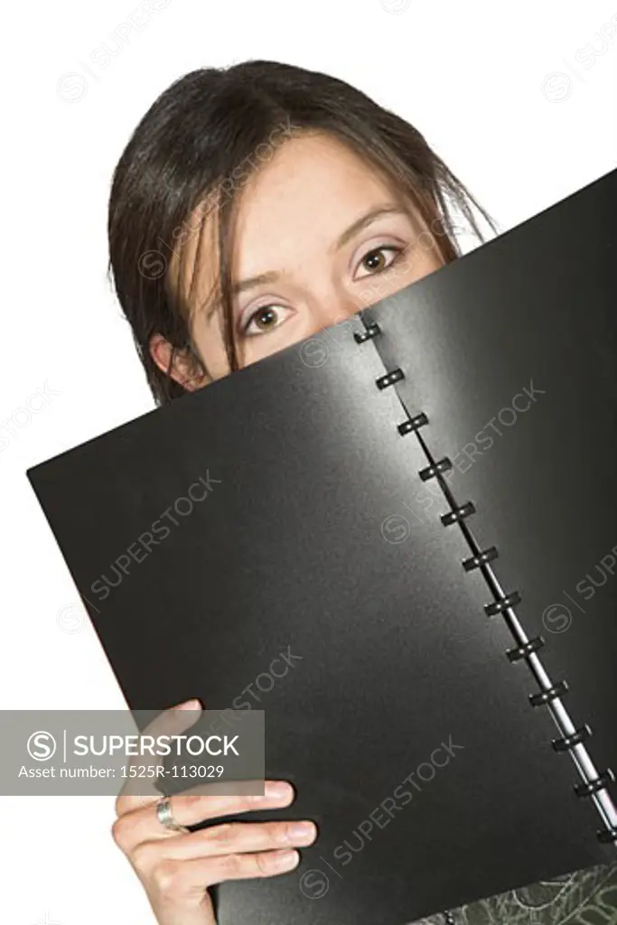 beautiful teen peeping over notebook over white