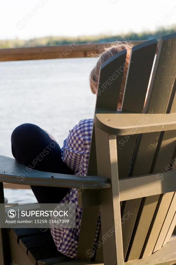 Teenage girl sitting in an Adirondack chair, Lake of the Woods, Ontario, Canada