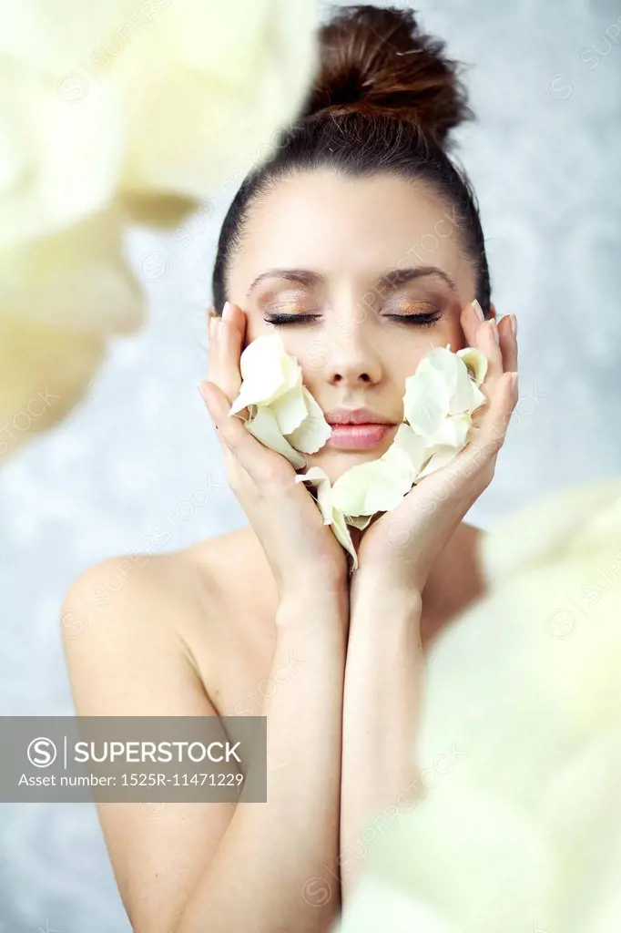 Pretty brunette lady holding petals close to face