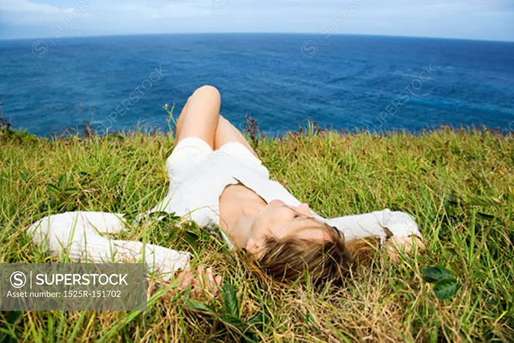 Portrait of young redheaded woman relaxing in grass above the ocean in Maui, Hawaii. 