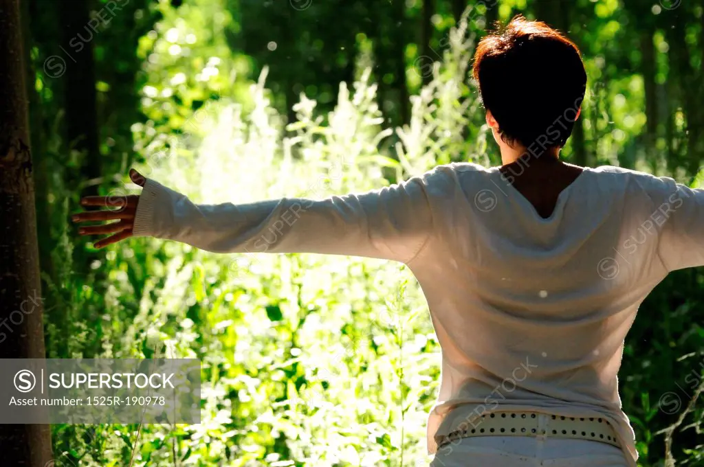 Woman with arms out stretched in green woodland