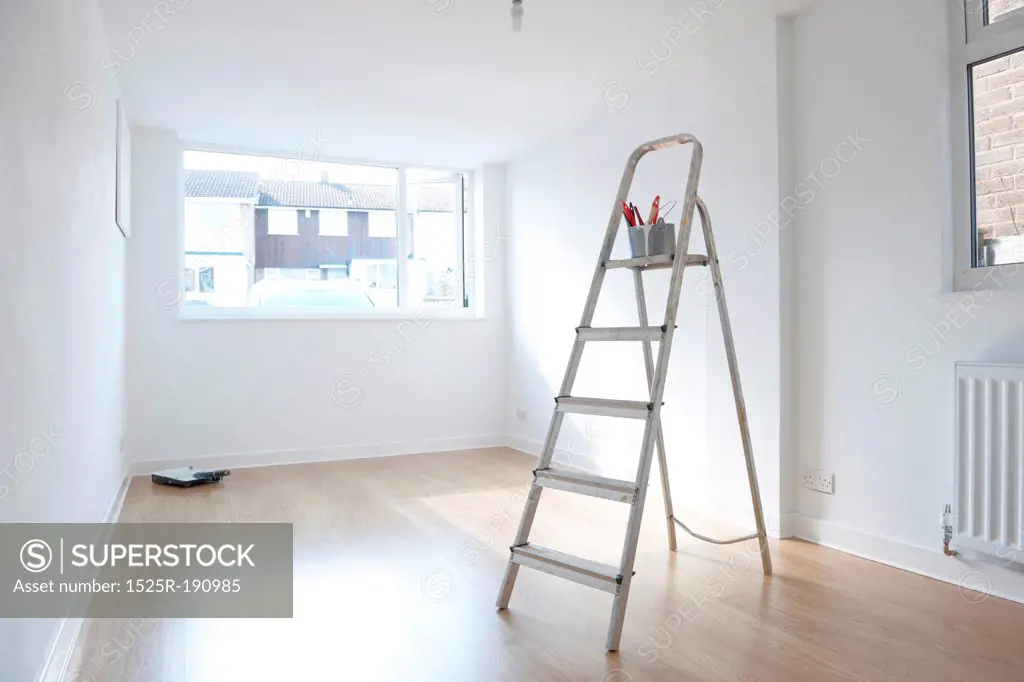 ladder with paint pot and brushes standing in empty room