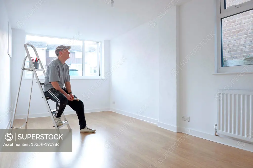 man sitting on ladder looking at newly decorated white painted room