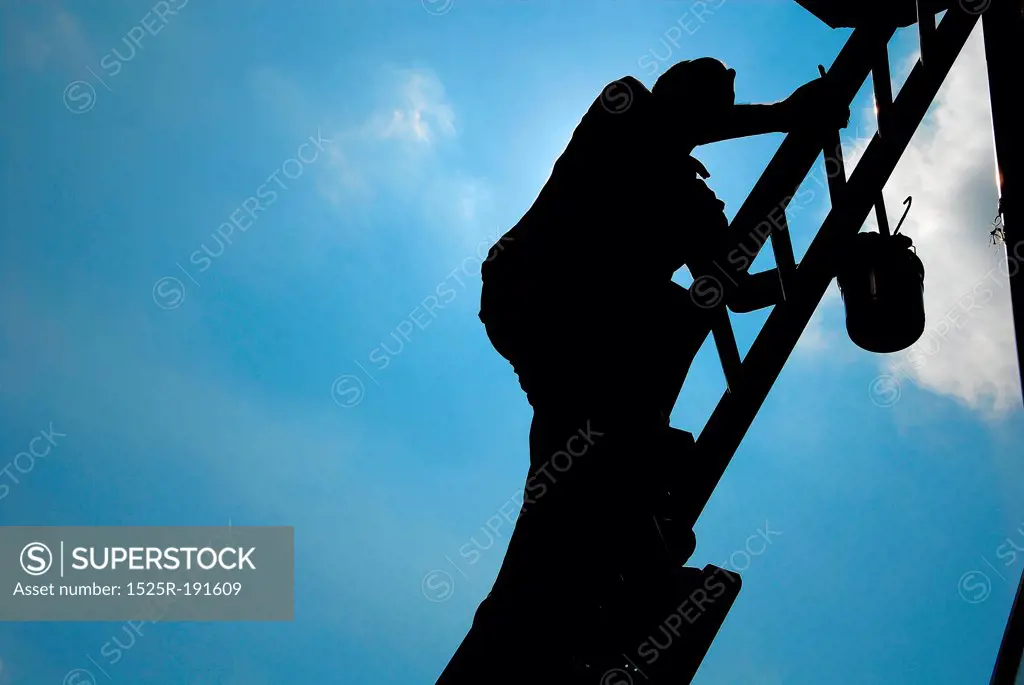 Silhouette of man climbing ladder to paint building