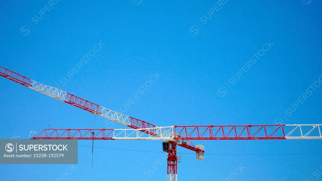 Red and White construction cranes against blue sky.
