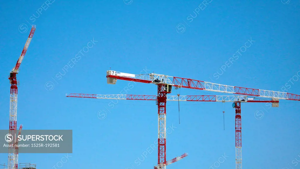 Red and White construction cranes against blue sky.
