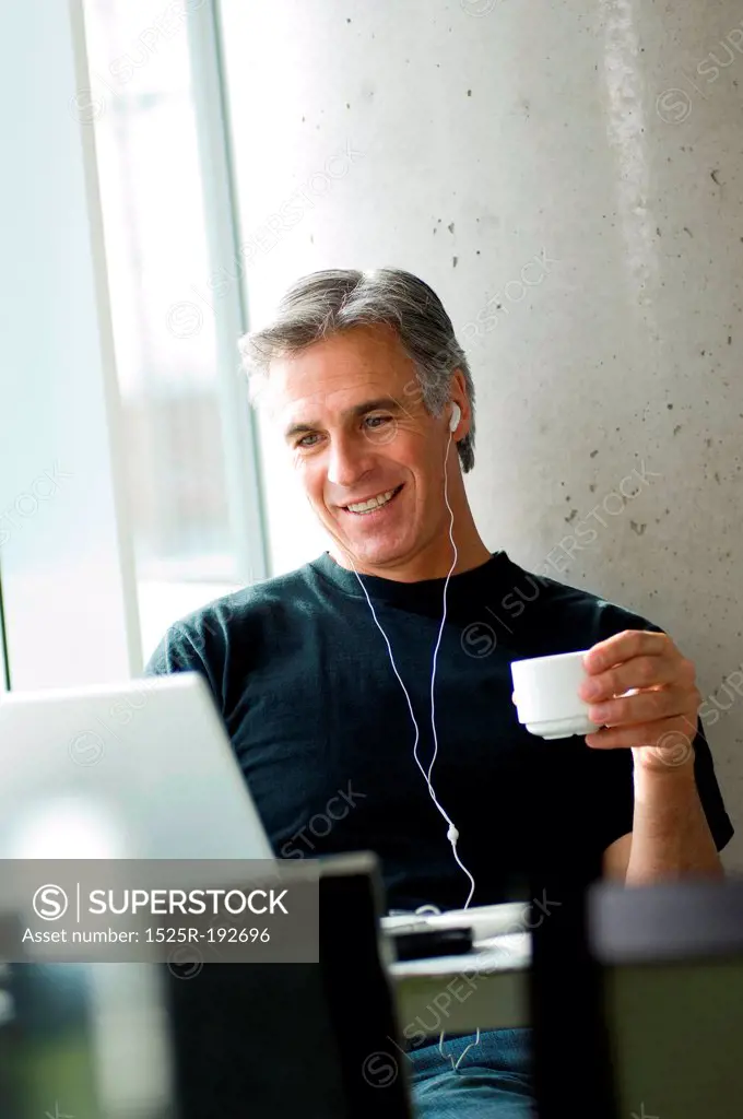 Middle-aged man listening to music in urban cafe.