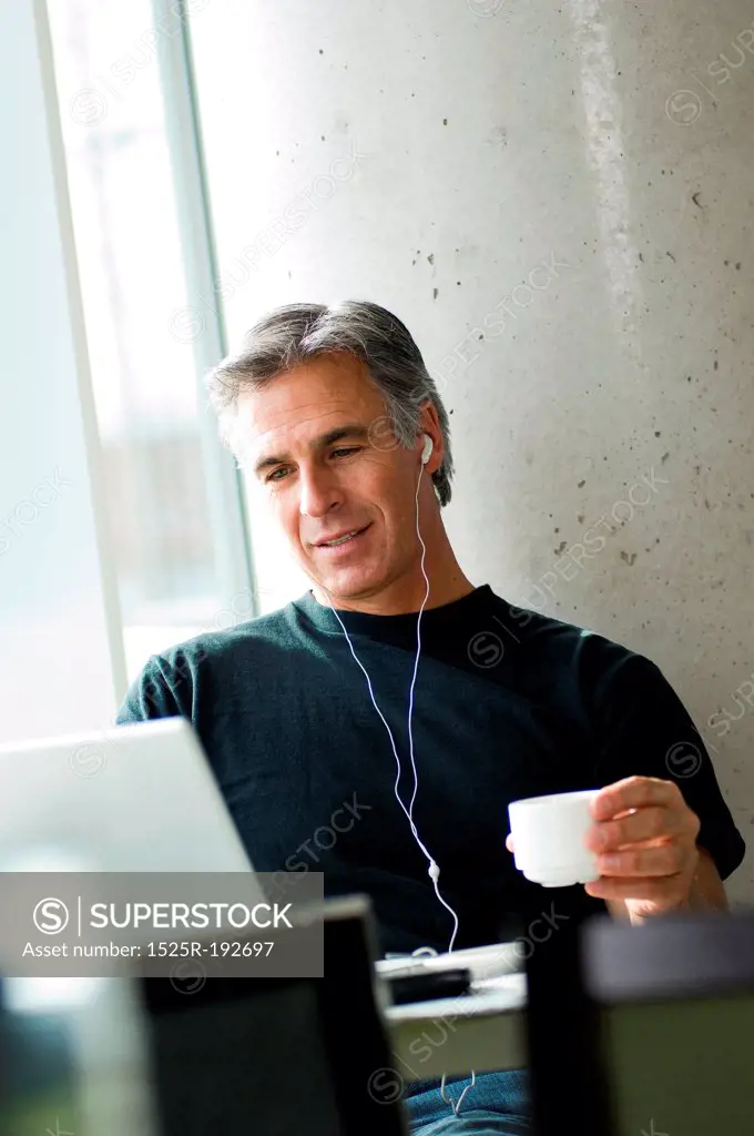 Middle-aged man listening to music in urban cafe.
