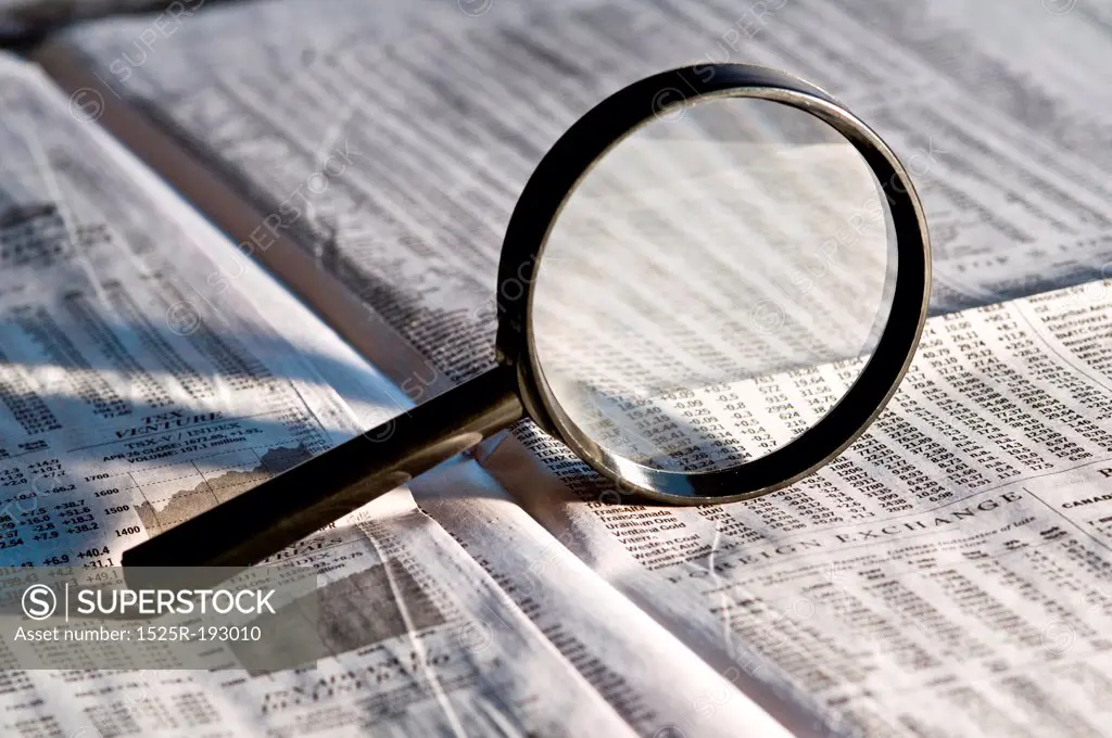 Magnifying glass highlighting investment stock quotes in business section of newspaper.