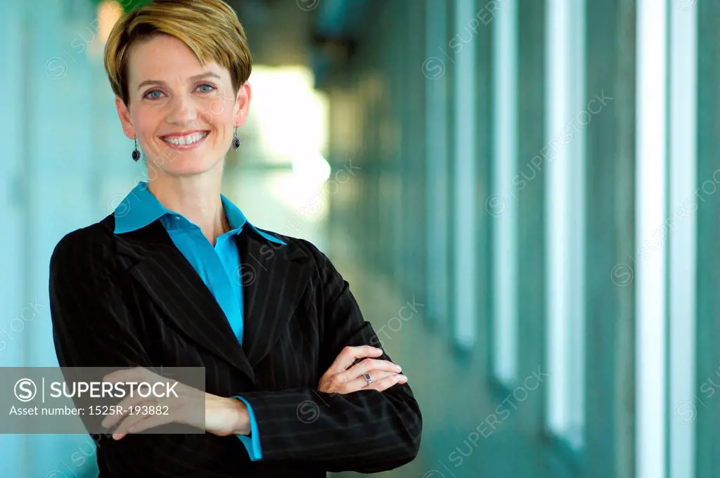Professional female executive folding arms while standing in hallway.