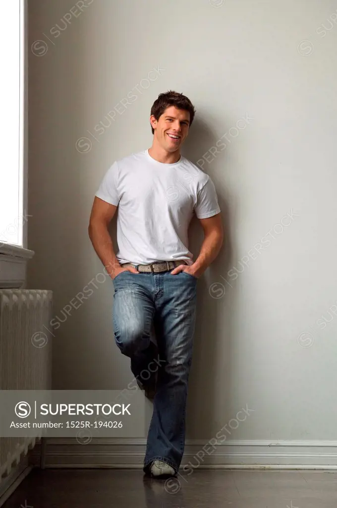 Young adult man leaning against white wall, wearing a white t-shirt.
