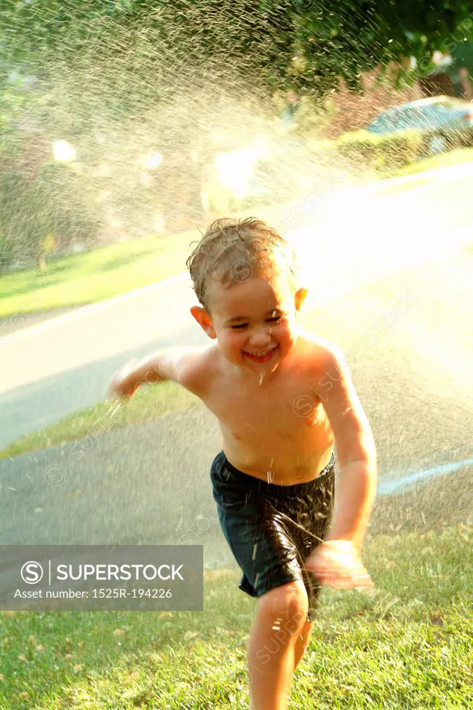 Young boy running through summer sprinkler.