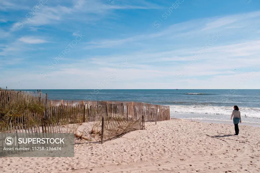 Woman walking along fencing on the beach in the Hamptons
