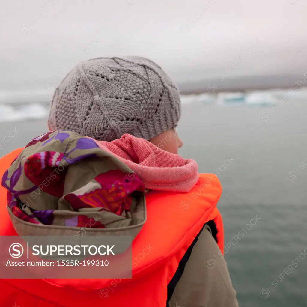 Girl in fluorescent orange life preserver, on glacial lake with icebergs