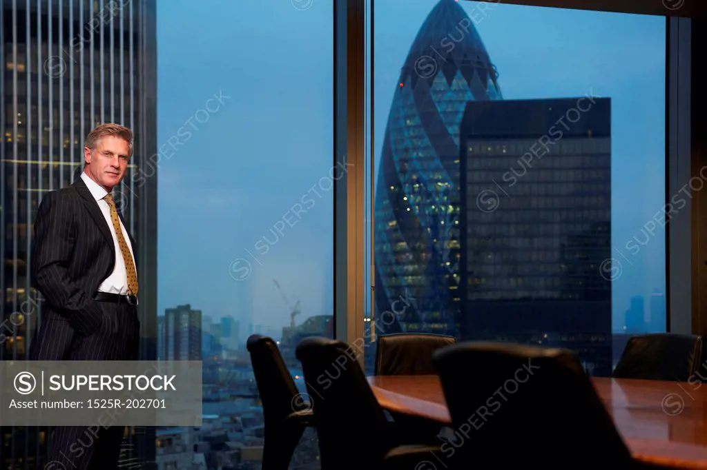 Business man standing next to table in boardroom looking at camera