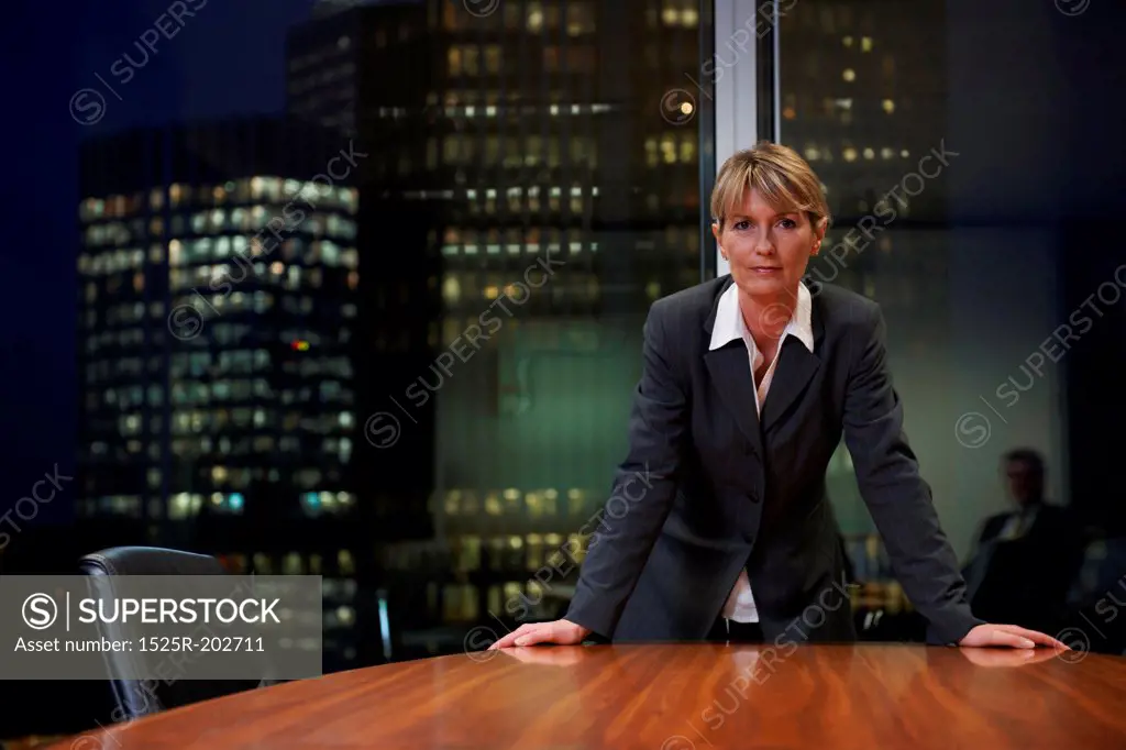 Senior Business woman leaning on table in boardroom looking at camera