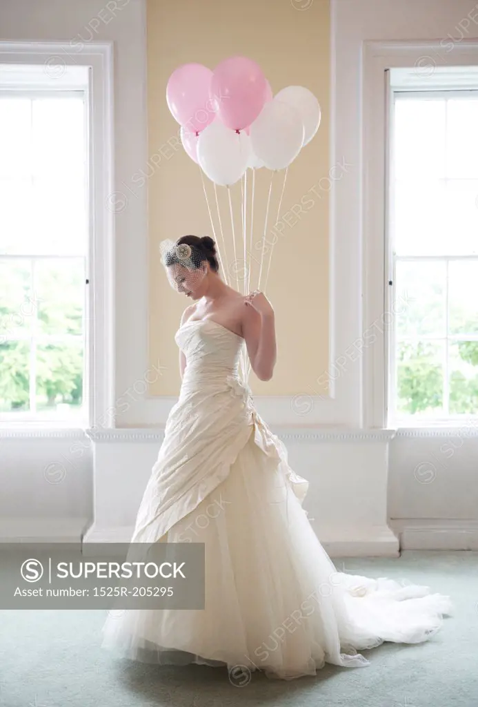 pretty bride in her wedding dress holding ballons in front of windows