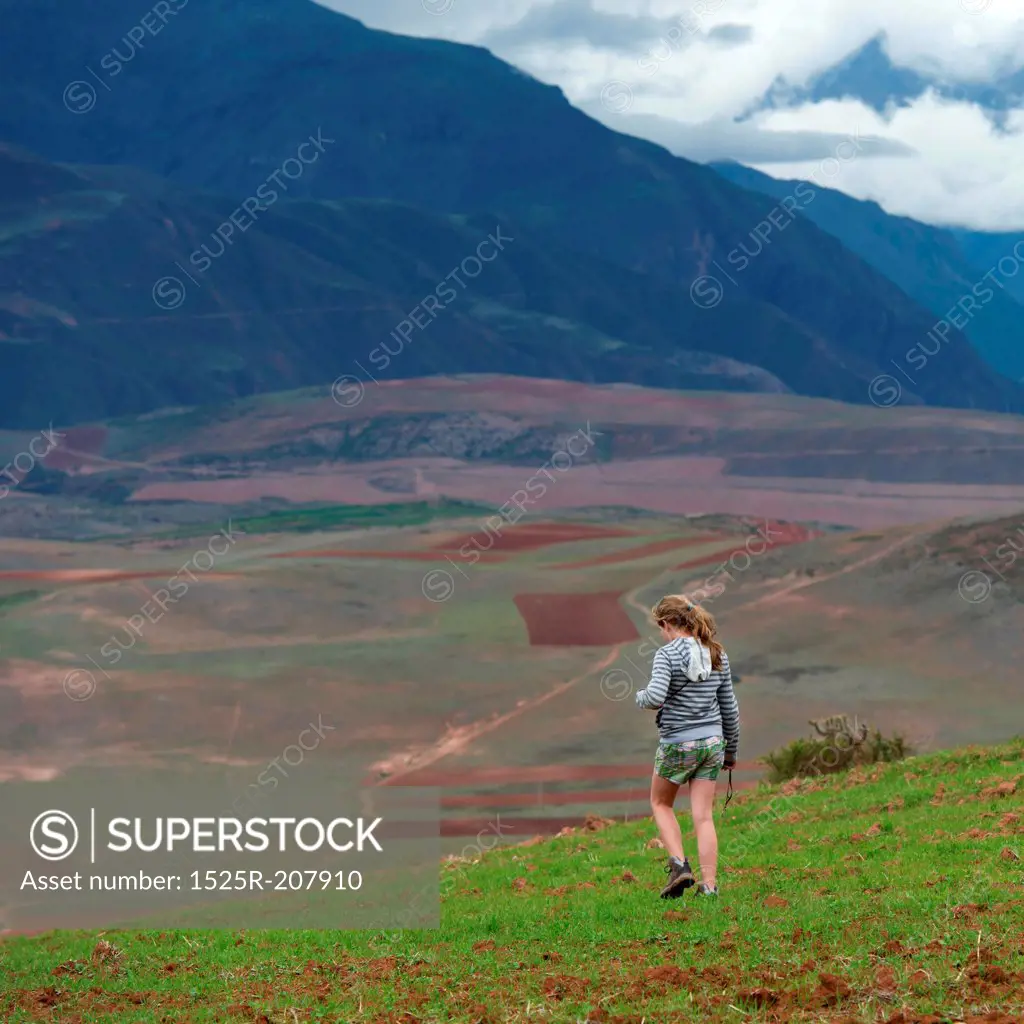 Teenage girl walking in a field with Sacred Valley in the background, Cusco Region, Peru
