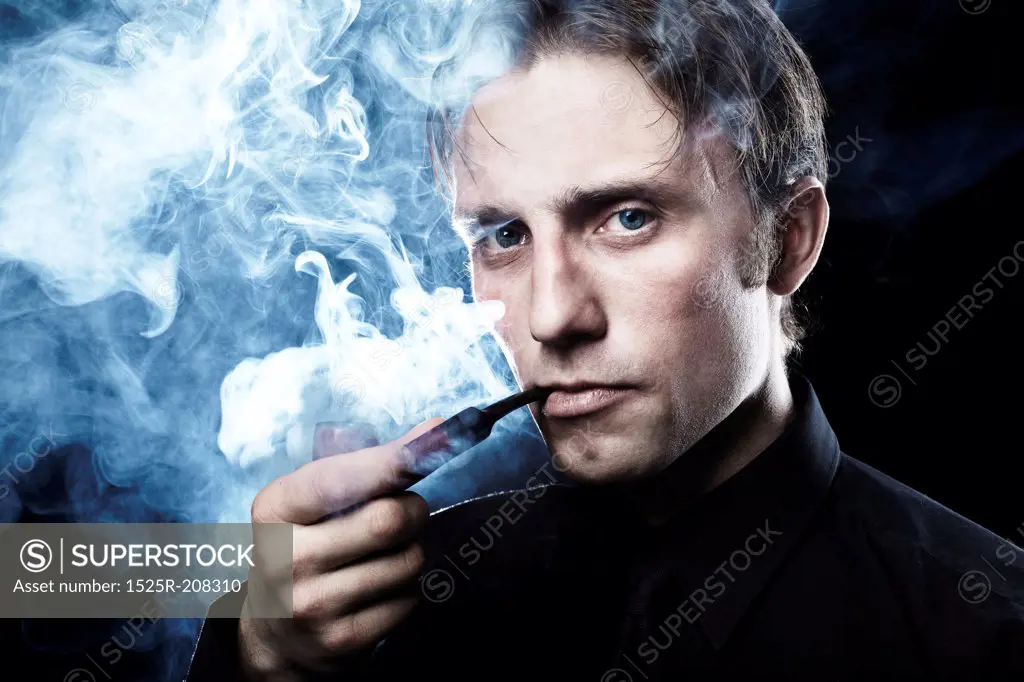 Artistic dark portrait of the young beautiful man. The young man smokes a tube