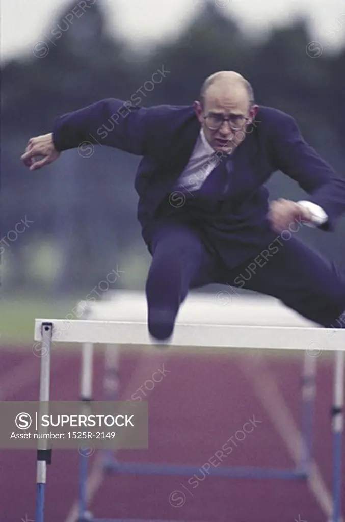 suited man jumping hurdles on running track